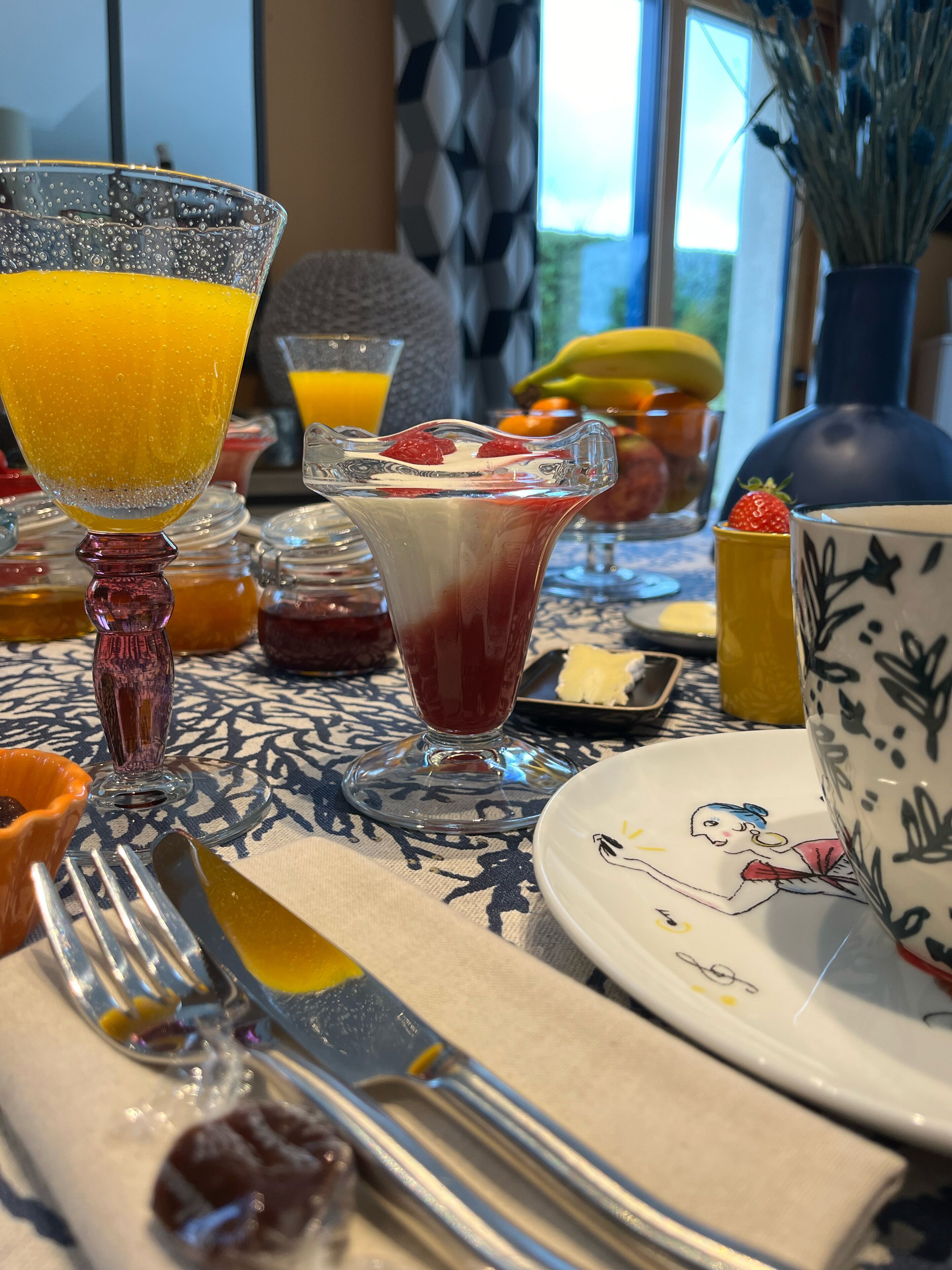 A dining table with various food items and drinks, including a glass of orange juice, a glass of red drink, and a plate with a cartoon character.