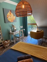 Quarto com cama, escrivaninha, cadeira, luminária pendente e vista para o verde lá fora.