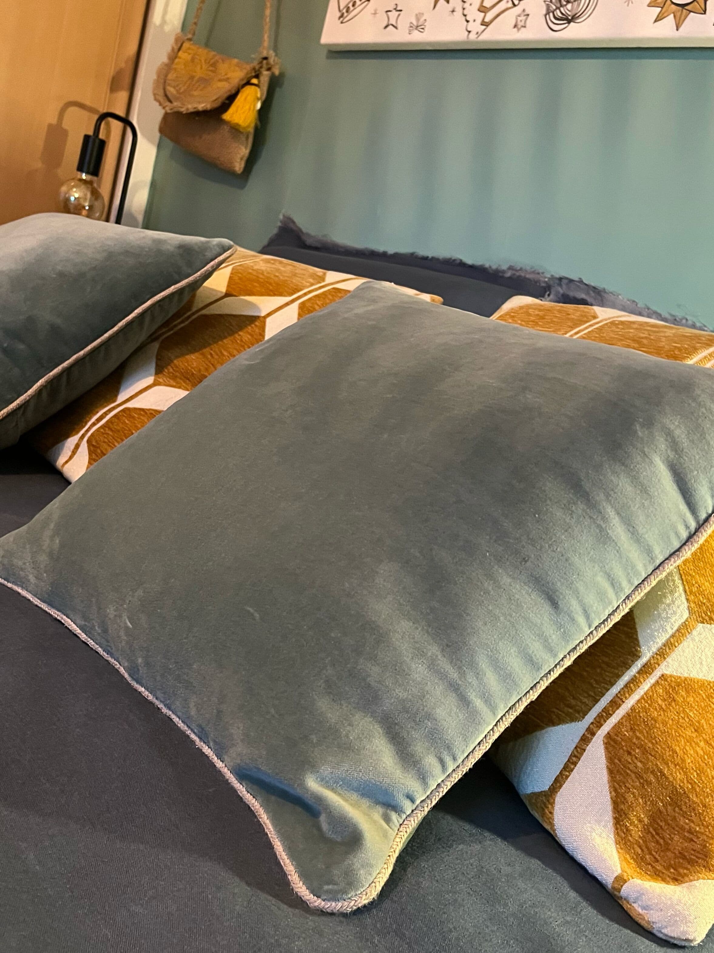 A bed with two pillows, a patterned blanket, and a wall with a decorative piece.