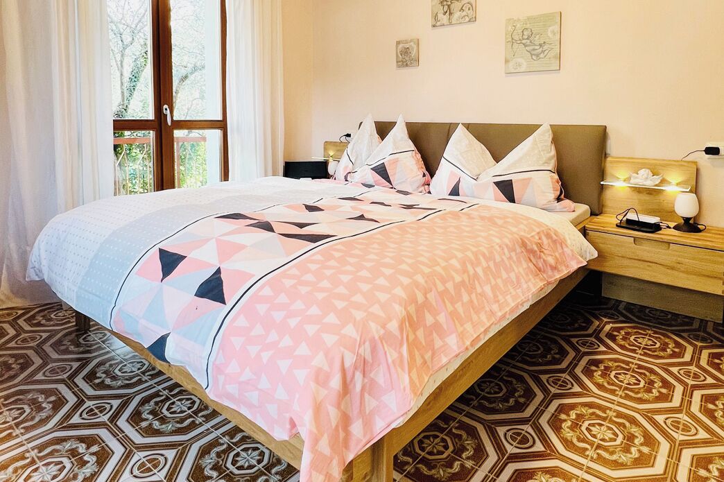 Un lit bien fait, recouvert d’une couvre-lit à motifs, une table de chevet avec une lampe et une fenêtre avec des rideaux.