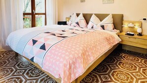 A neatly made bed with a patterned bedspread, a bedside table with a lamp, and a window with curtains.