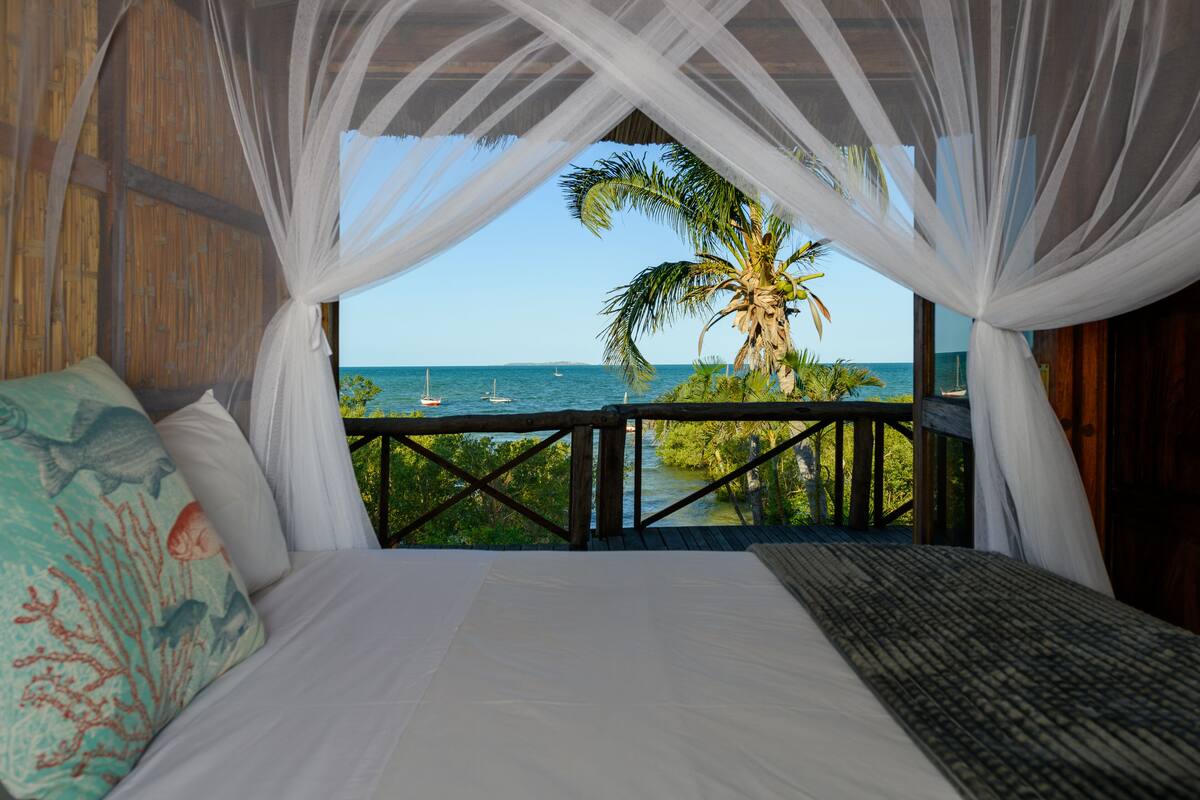 A bedroom with a view of the sea, a palm tree, and a boat.