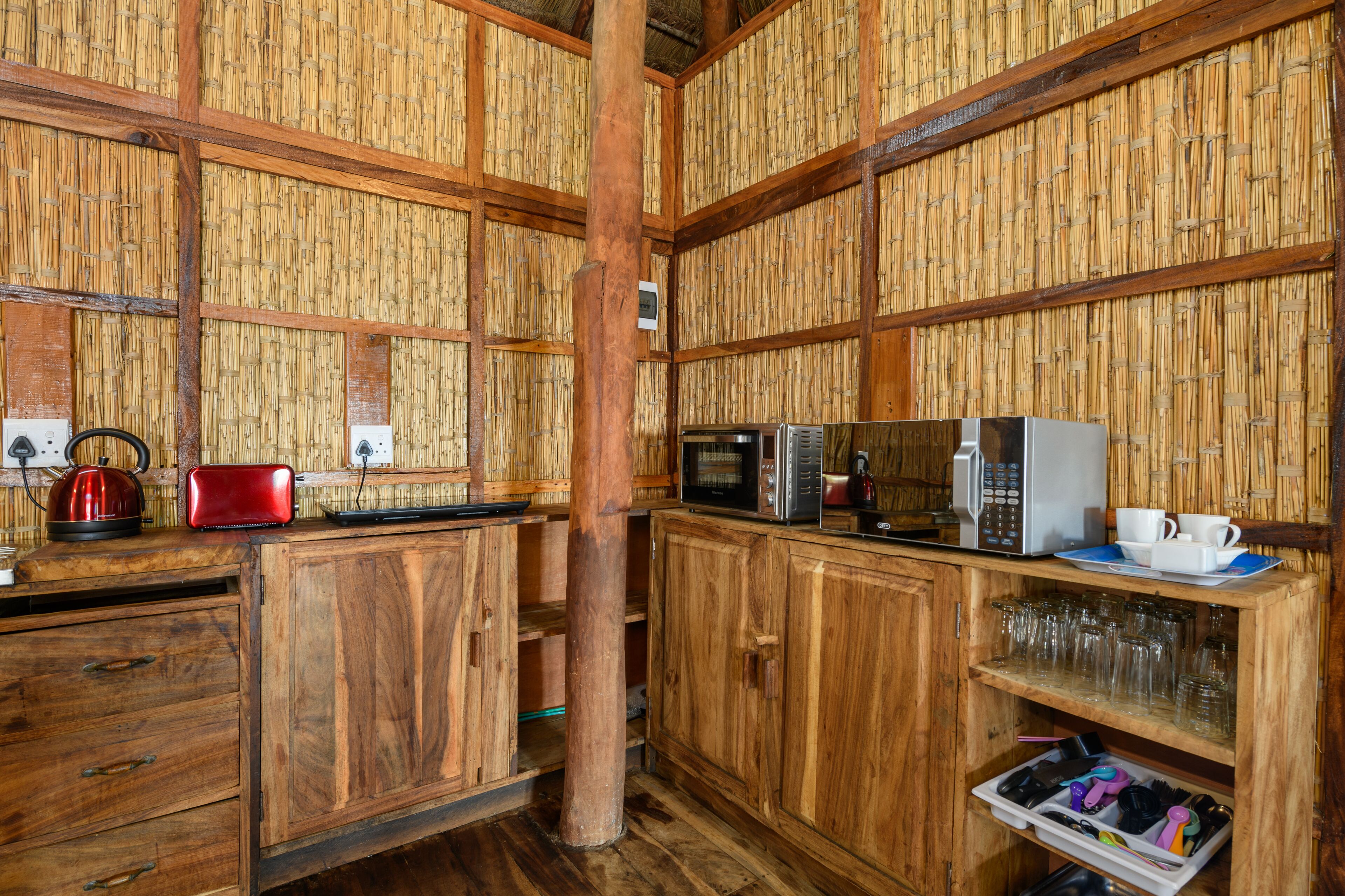 A rustic kitchen with wooden cabinets, a microwave, a kettle, and a coffee maker.