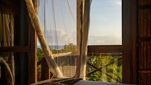 A room with a bed, a window with a view of greenery, and a wooden structure. - Ocean Pearl Beach Lodge (Vilanculos)