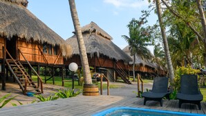 A pool area with wooden deck, thatched-roof huts, and lounge chairs. - Ocean Pearl Beach Lodge (Vilanculos)