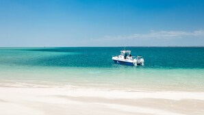 A boat on a clear turquoise sea with a sandy beach in the foreground. - Ocean Pearl Beach Lodge (Vilanculos)