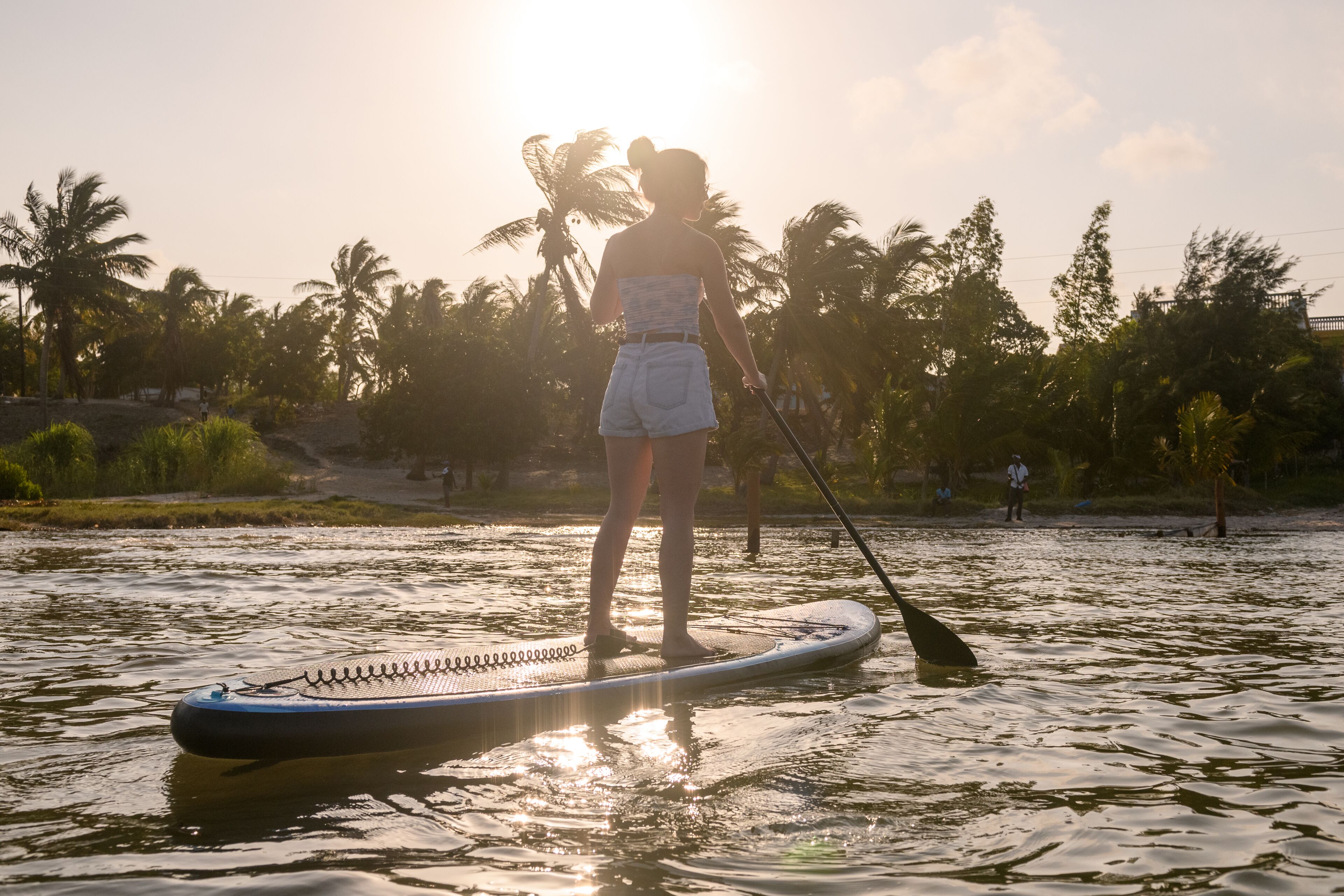 A person standing on a paddleboard in a body of water with palm trees in the background.