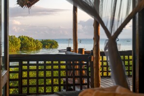 Eine Holzdielen-Terrasse mit Blick aufs Meer und ein Reetdachgebäude.