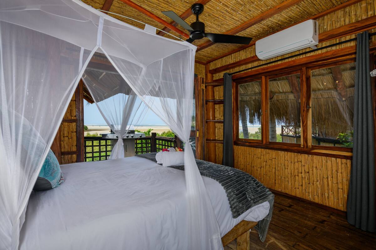 A room with a bed, a ceiling fan, and a window with a view.