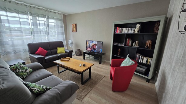 Ett vardagsrum med en soffa, en röd fåtölj, ett soffbord, en tv och en bokhylla.