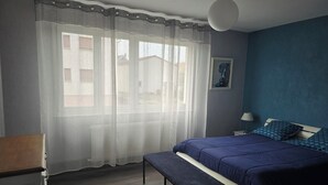 Ett sovrum med en säng, en bänk, ett sängbord, en lampa och en tavla på väggen.