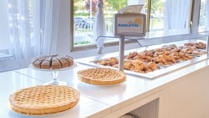A bakery display with various baked goods, including cakes and pastries, in a bright room with large windows. - Family Hotel Alexander (Jesolo)