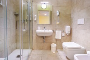 A modern bathroom with a glass shower enclosure, a sink with a mirror above it, a toilet, and a hand dryer. - Family Hotel Alexander (Jesolo)