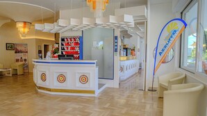 A reception area with a modern design, featuring a reception desk, seating area, and a large window providing natural light. - Family Hotel Alexander (Jesolo)