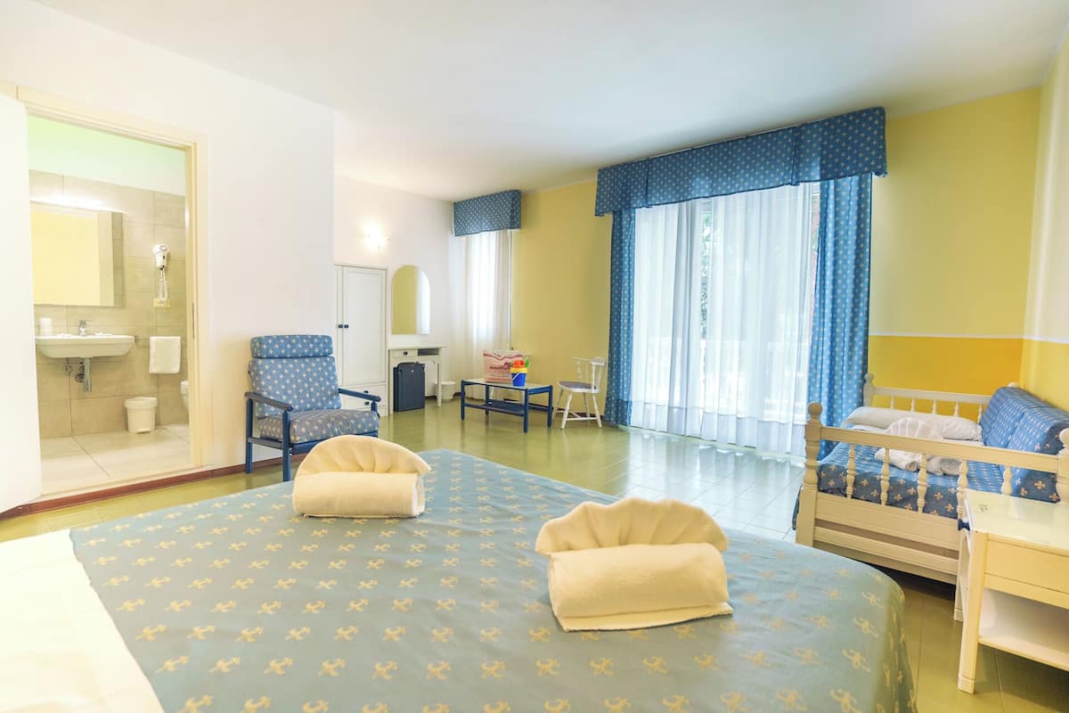 A hotel room with a bed, two chairs, a desk, a bathroom, and a window with curtains.