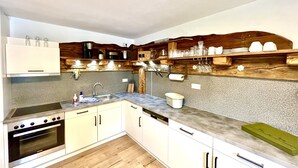 A modern kitchen with white cabinets, a stainless steel oven, a dishwasher, and wooden shelves above the counter.