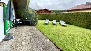 A patio with a table and chairs, a lounge area with sun loungers, and a neatly trimmed hedge.