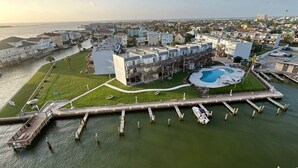 An aerial view of a coastal residential area with a marina, a swimming pool, and a large building with multiple balconies.