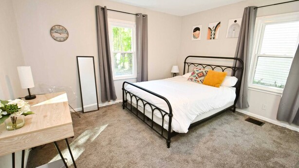 Een slaapkamer met een bed, een bureau, een stoel, een raam en een klok aan de muur.