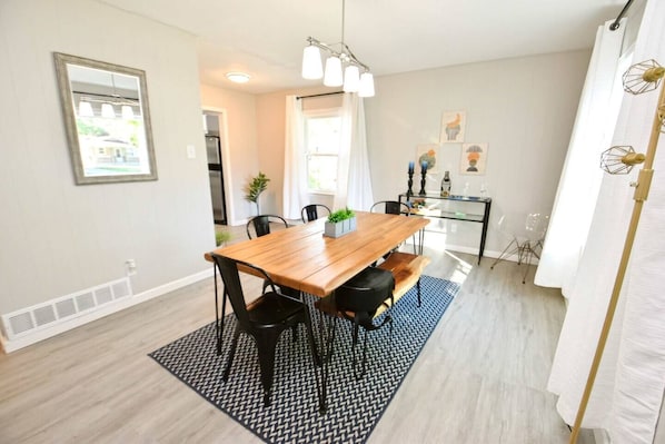 Un espace repas comprenant une table en bois, des chaises noires, un tapis à motifs et un luminaire suspendu au plafond.
