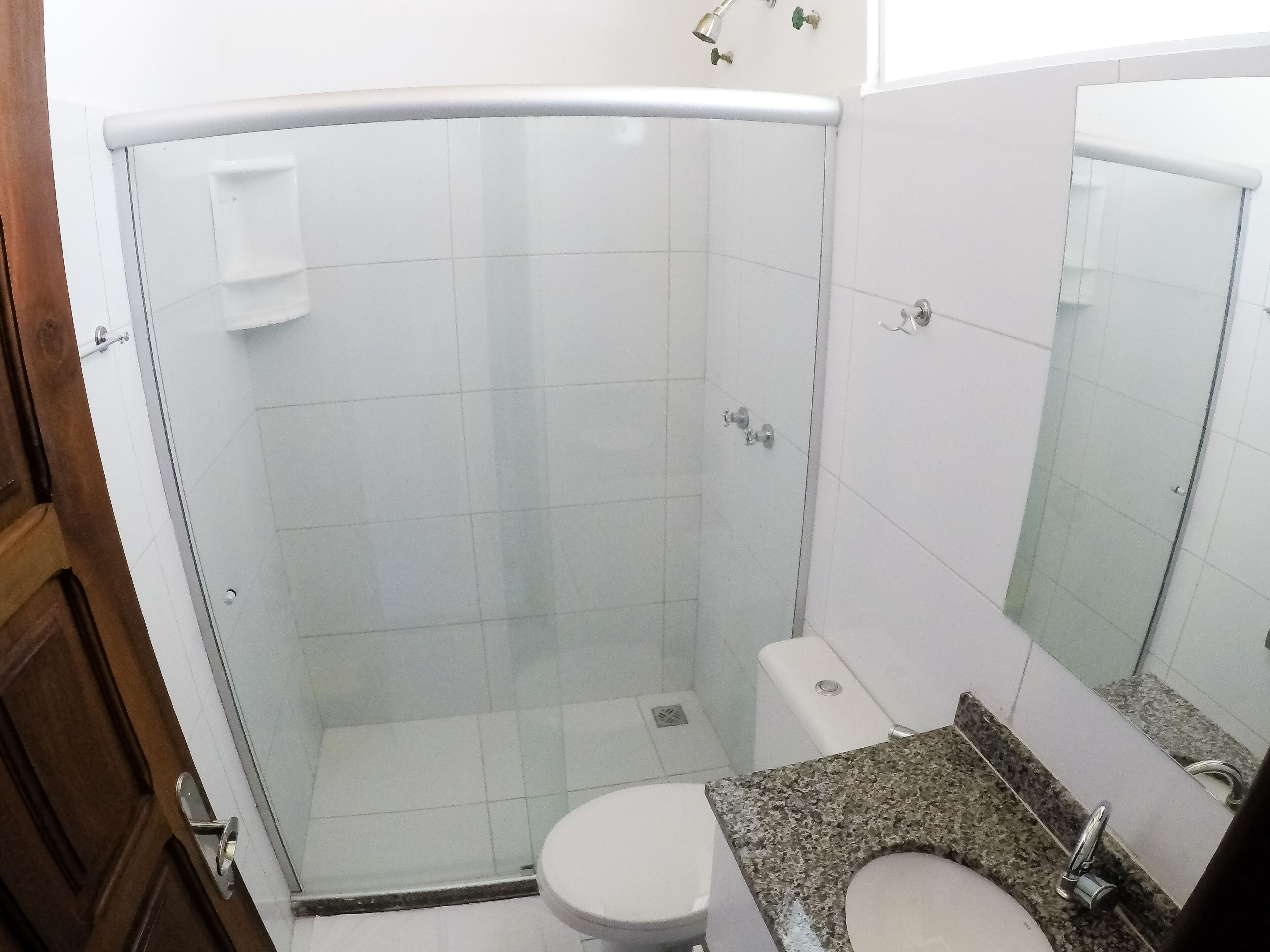Un baño con ducha envuelta en vidrio, inodoro blanco y encimera de granito con lavamanos.