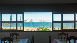 A room with a view of the beach and the sea through large windows. There are two tables with chairs, and the room has a simple, clean design. - Brisa do Caita Praia Hotel (Cairu)