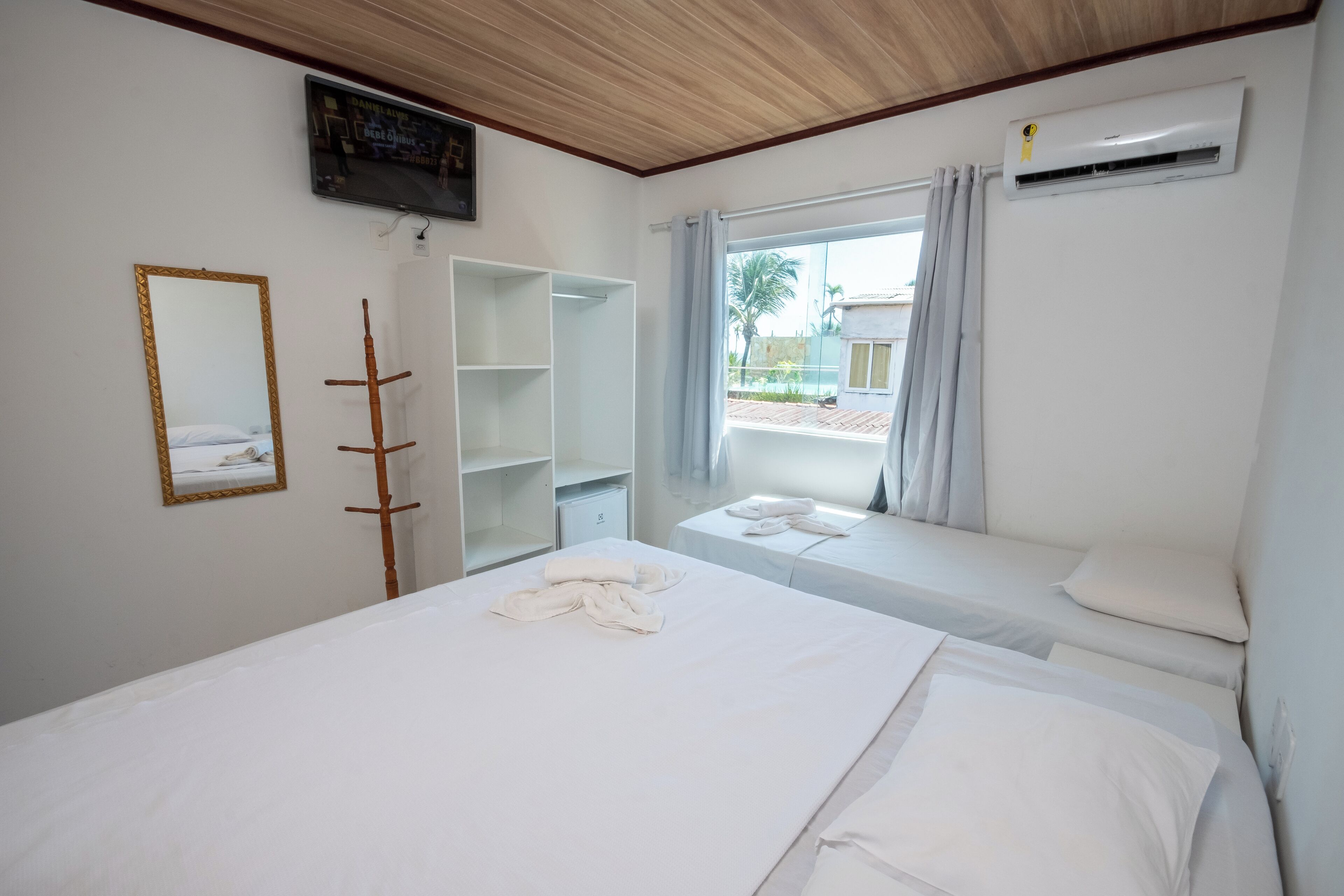 A hotel room with a bed, a TV, a wardrobe, and a window with a view of the outside.
