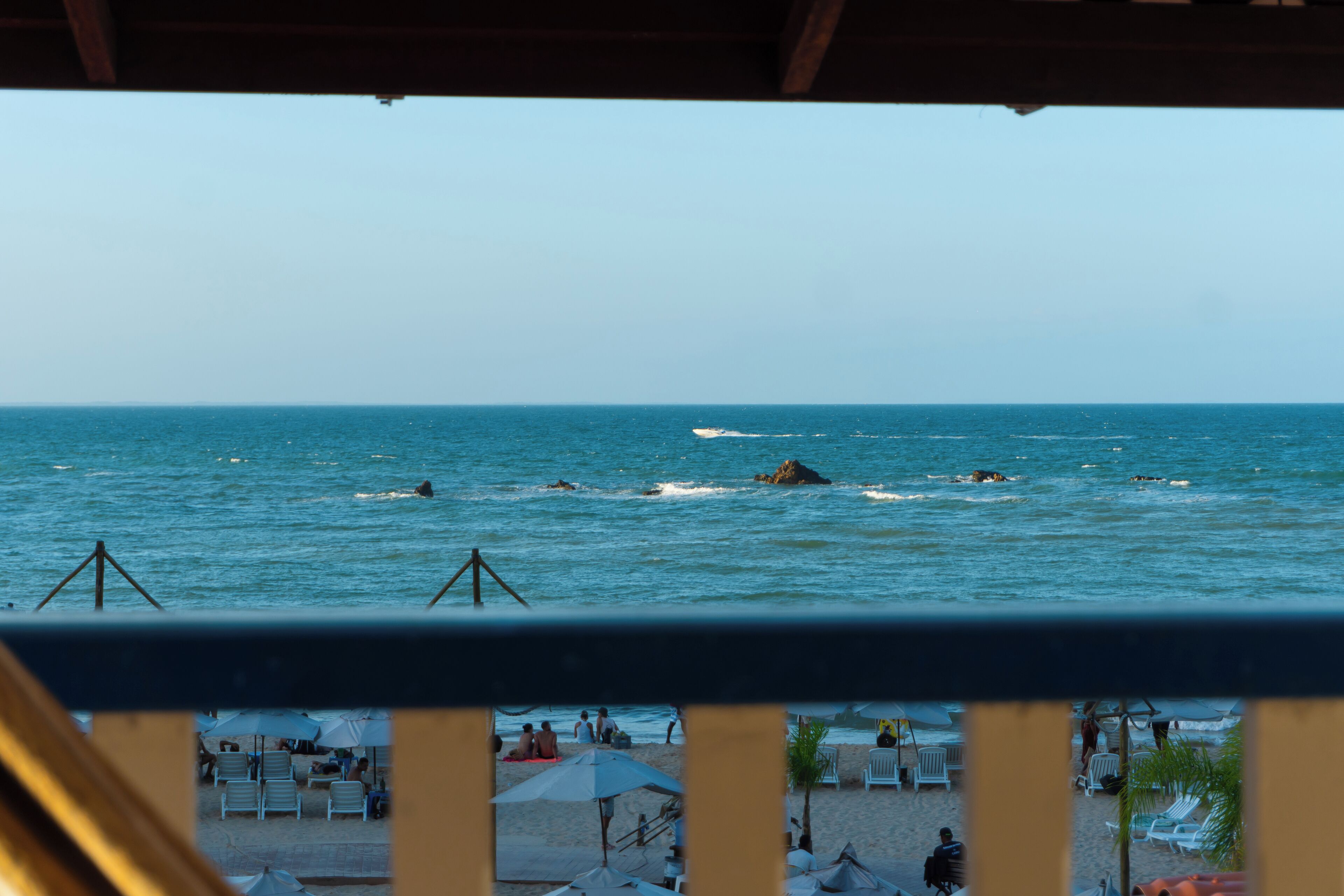 Vista da praia a partir de uma varanda com grades, ondas do oceano e cadeiras e guarda-sóis de praia.