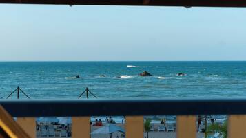 Vista da praia a partir de uma varanda com grades, ondas do oceano e cadeiras e guarda-sóis de praia.