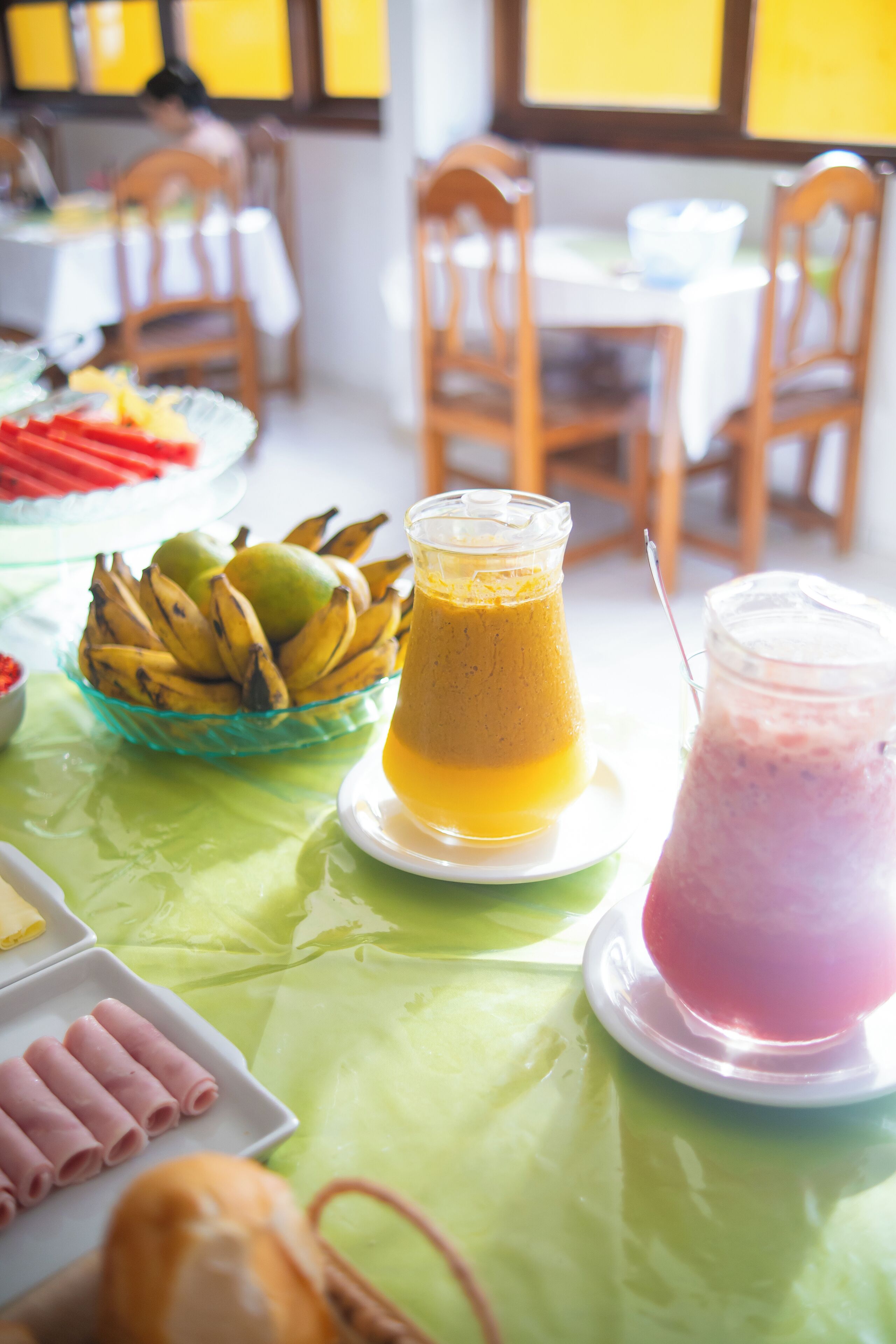 A table with a green tablecloth, a bowl of bananas, a pitcher of orange juice, and a pink smoothie.