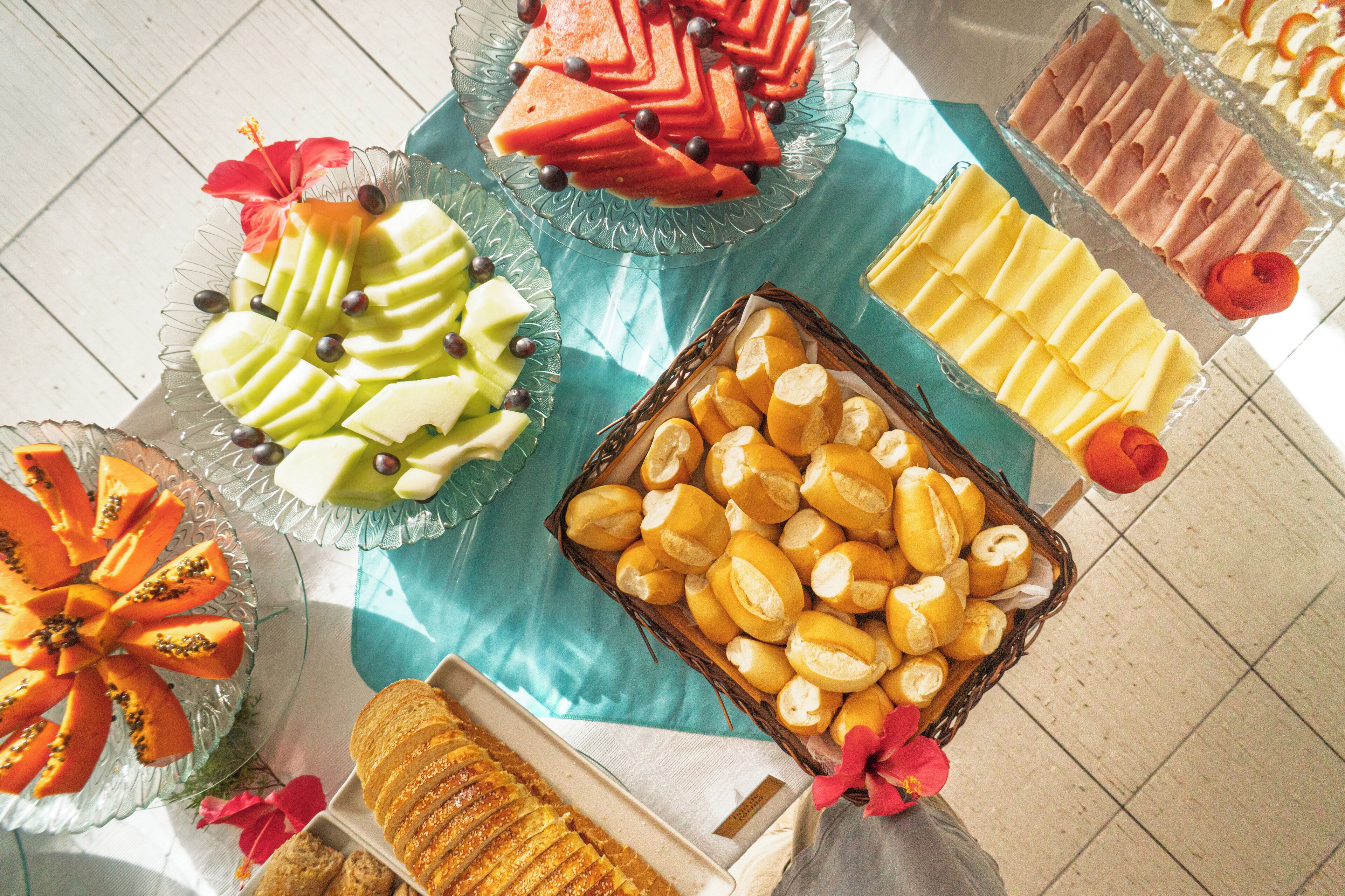 Variedad de alimentos dispuestos en una mesa, incluyendo frutas cortadas, pasteles y pan.