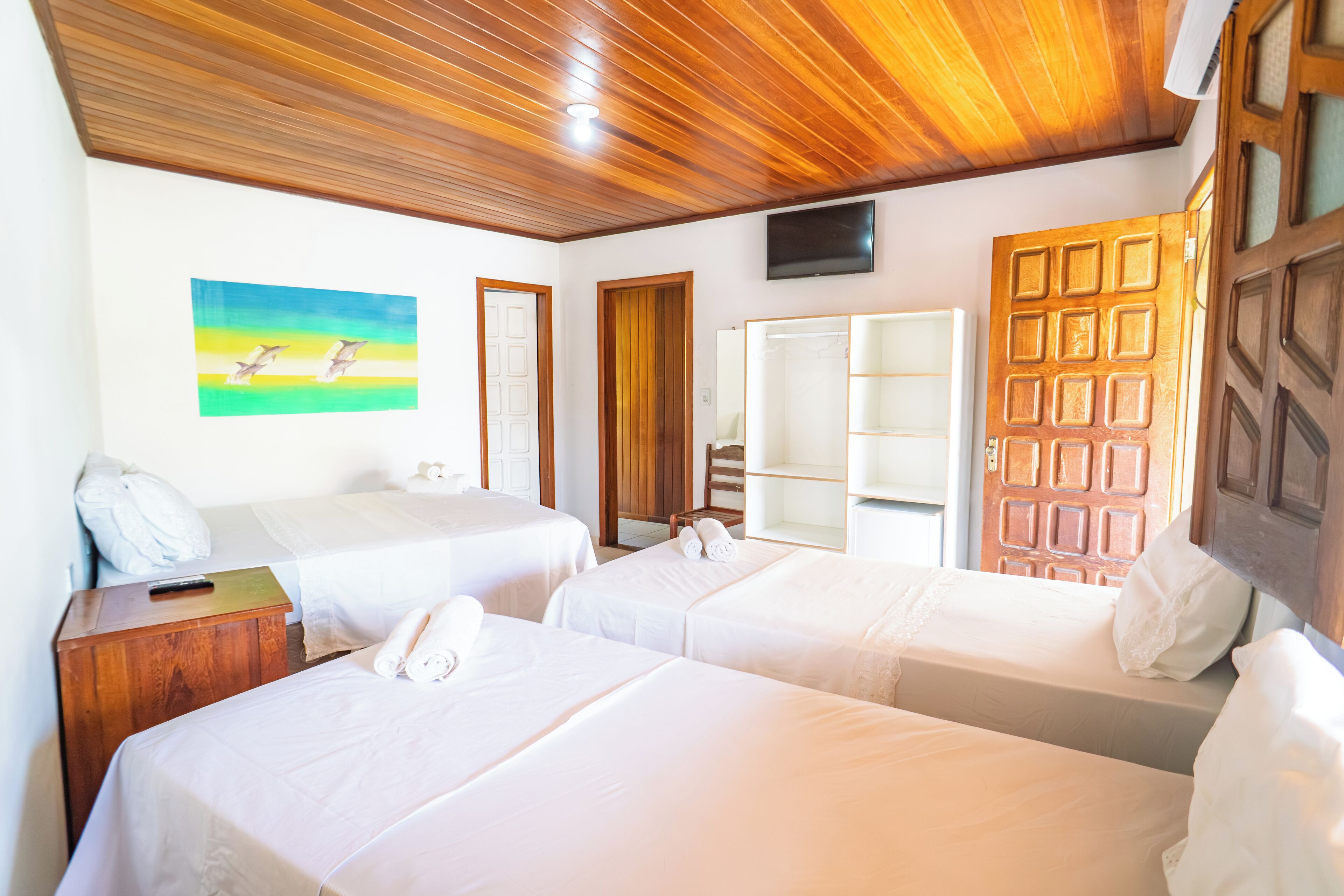 A hotel room with two single beds, wooden headboards, a wooden ceiling, a painting on the wall, and a television mounted above a wooden door.