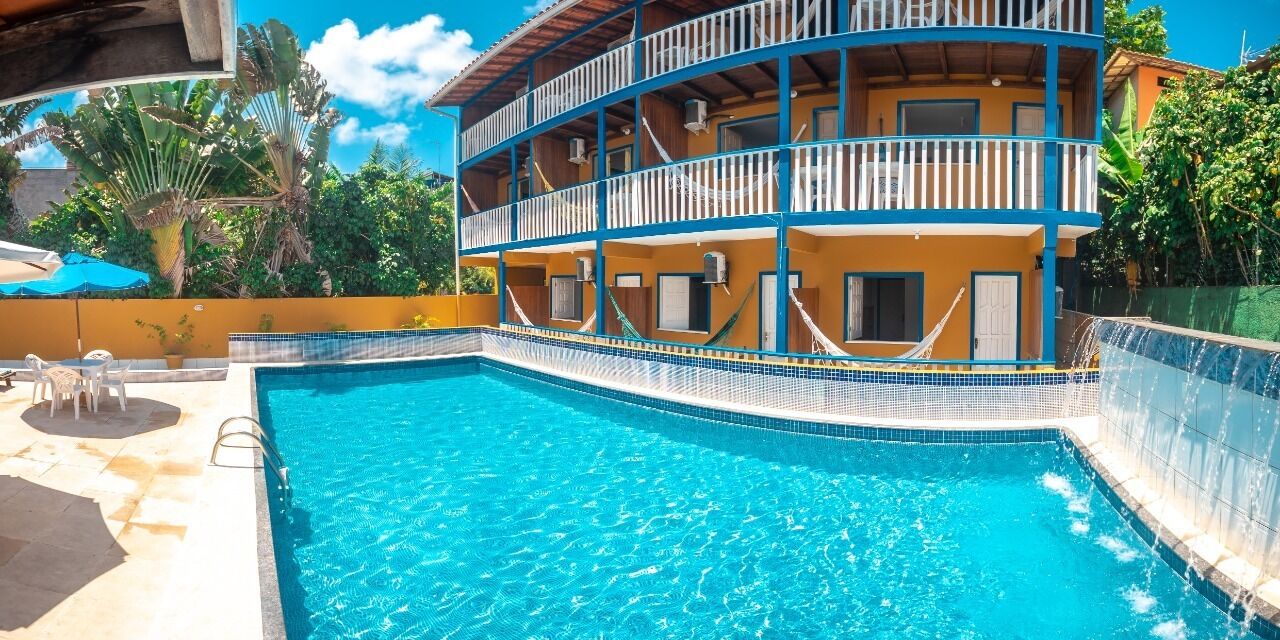 A two-story building with a swimming pool, outdoor seating, and a view of the surrounding greenery.