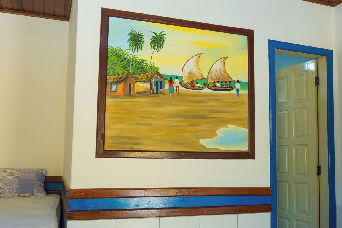 Una habitación con una cama, un cuadro de una playa y una puerta.