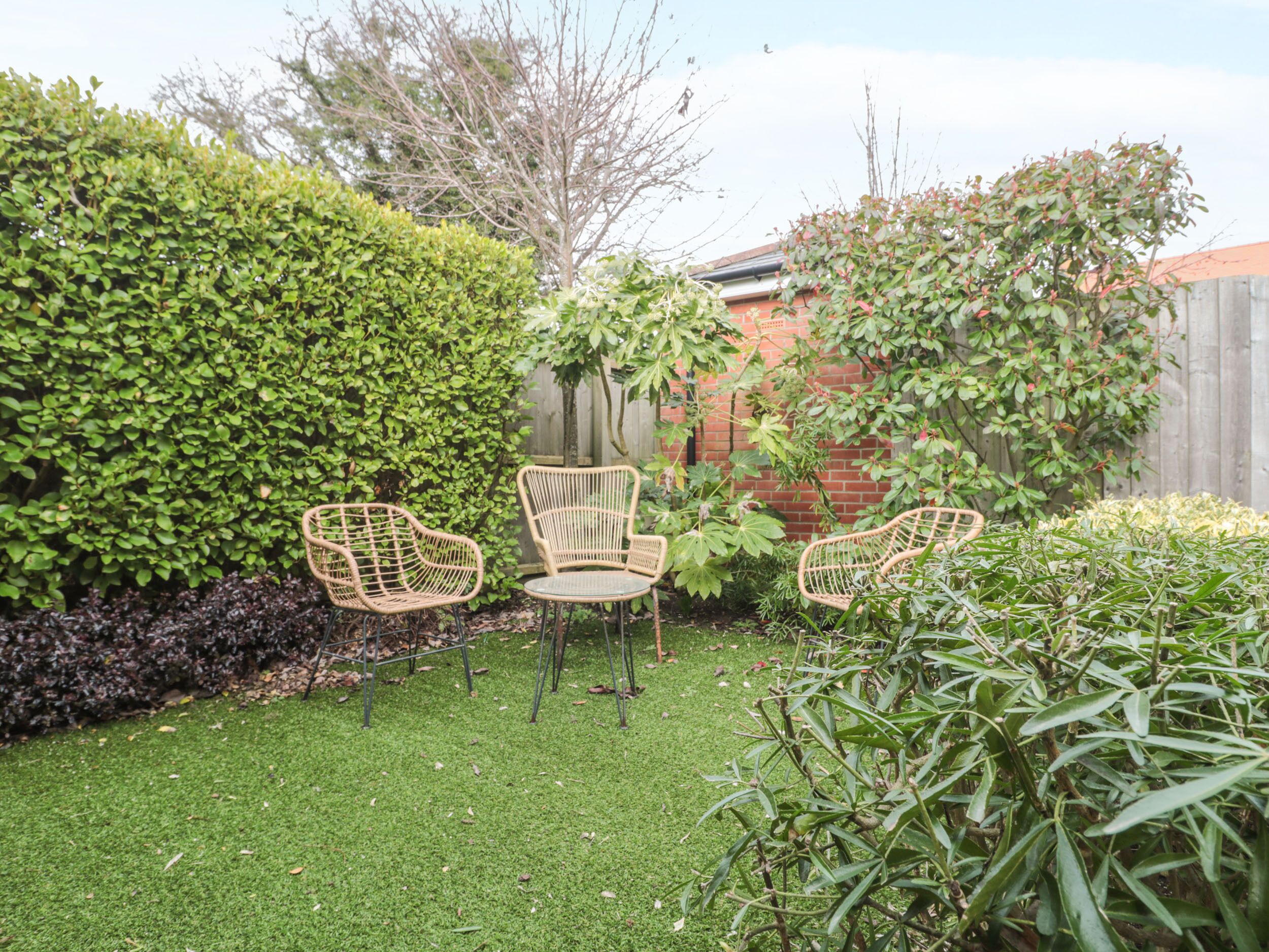 Un jardin avec trois chaises en osier, une petite table ronde et diverses plantes.