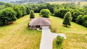Ein Luftbild eines Hauses mit Auffahrt zu einer Garage, umgeben von einem gepflegten Rasen und dichten Bäumen.