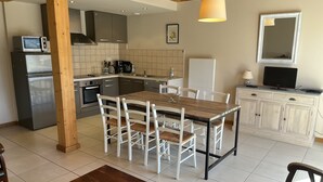 A modern kitchen with a dining area, featuring a wooden table, white chairs, a built-in oven, and a refrigerator. - Maison à Camparan Proche de Saint-lary (Camparan)