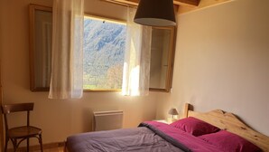 A bedroom with a bed, a chair, a window with curtains, a bedside lamp, and a radiator. - Maison à Camparan Proche de Saint-lary (Camparan)