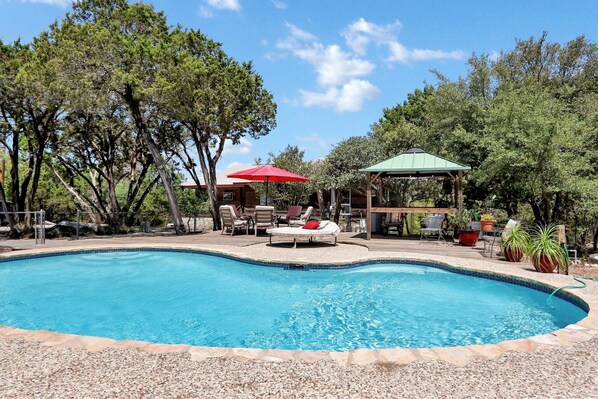 A swimming pool with lounge chairs and umbrellas, surrounded by trees and a gazebo. - Painted Paradise Main House I Private Pool I Lake Nearby (New Braunfels)