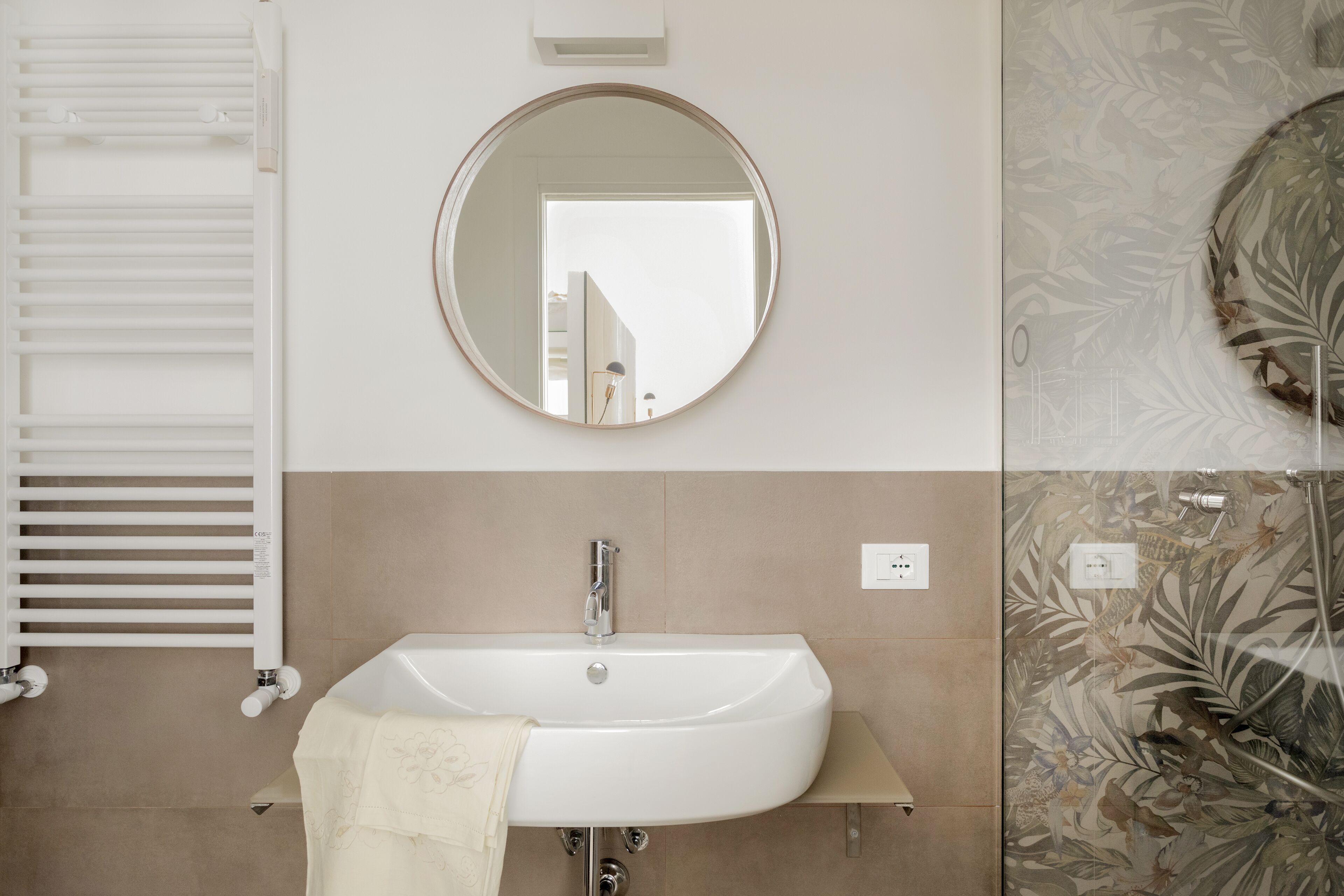 A bathroom with a white sink, a round mirror, and a towel hanging on the sink.