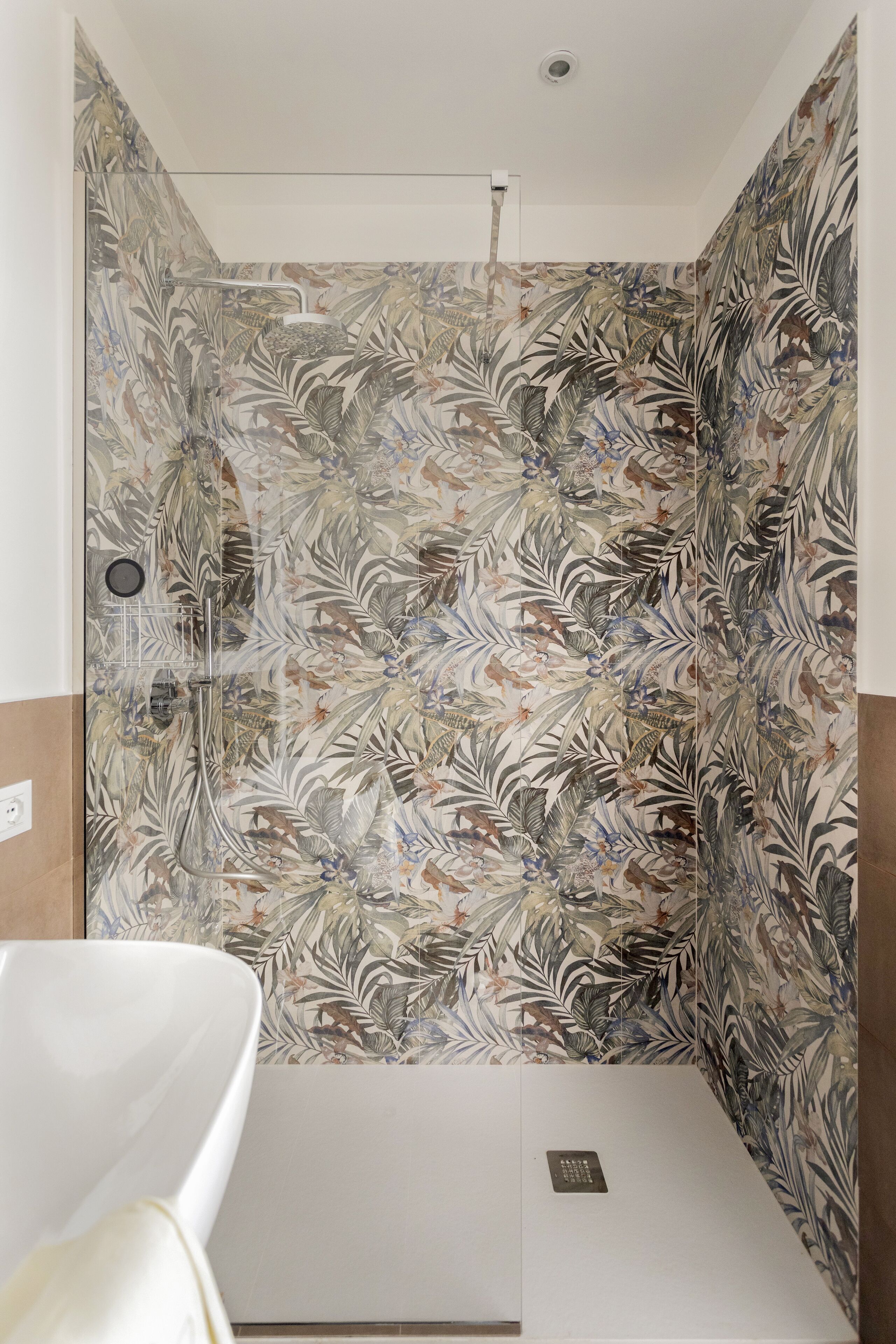 Una ducha con un estampado de azulejos florales, un lavamanos blanco y un panel de control en la pared.