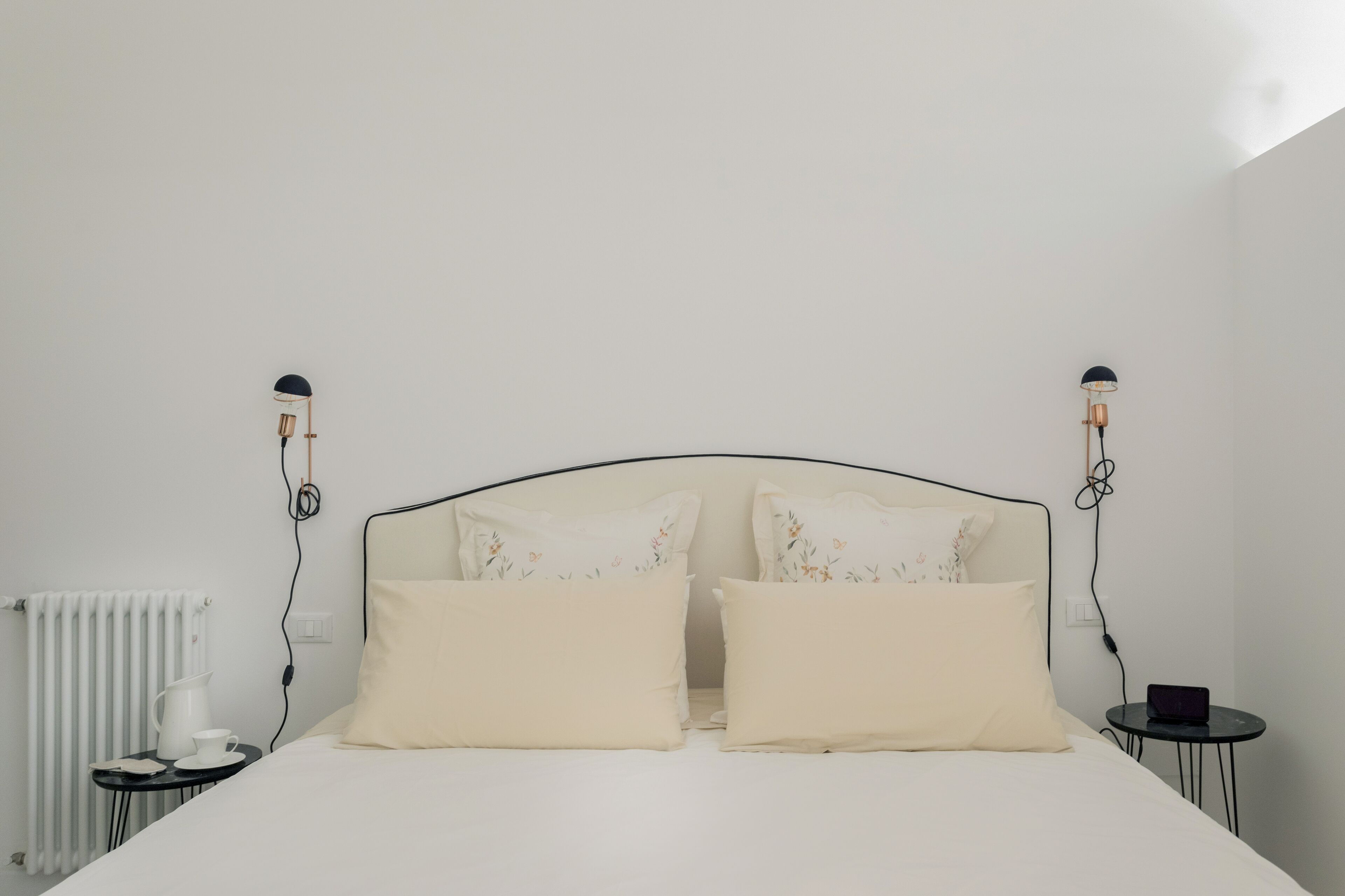 A neatly made bed with two pillows, a bedside table with a lamp, and a radiator.