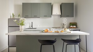 Une cuisine moderne avec des meubles gris, un plan de travail blanc et deux tabourets de bar noirs.