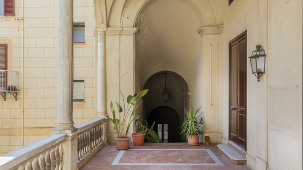 Un espace extérieur abrité, doté d’un sol carrelé, de plantes en pot, d’une rambarde et d’une porte.