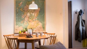 Un coin repas avec une table en bois, des chaises, une carte accrochée au mur et un porte-manteau avec des vestes.