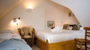 Une chambre confortable avec un plafond en pente, un lit en bois, une chaise en osier et une petite table en bois.
