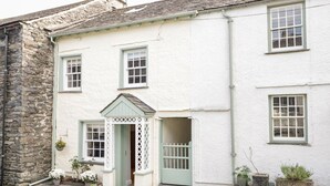 A white building with a stone facade, a small porch with a lattice door, and potted plants. - Jessamine Cottage (Ambleside)