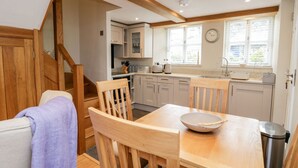 A modern kitchen with wooden cabinets, a dining table with chairs, and a staircase leading to another level. - Jessamine Cottage (Ambleside)