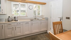 A modern kitchen with white cabinets, a wooden ceiling, a sink, and a dining area with a chair and table. - Jessamine Cottage (Ambleside)