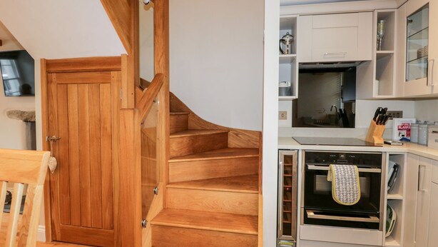 A wooden staircase leading to a kitchen with white cabinets, a stove, and a microwave. - Jessamine Cottage (Ambleside)